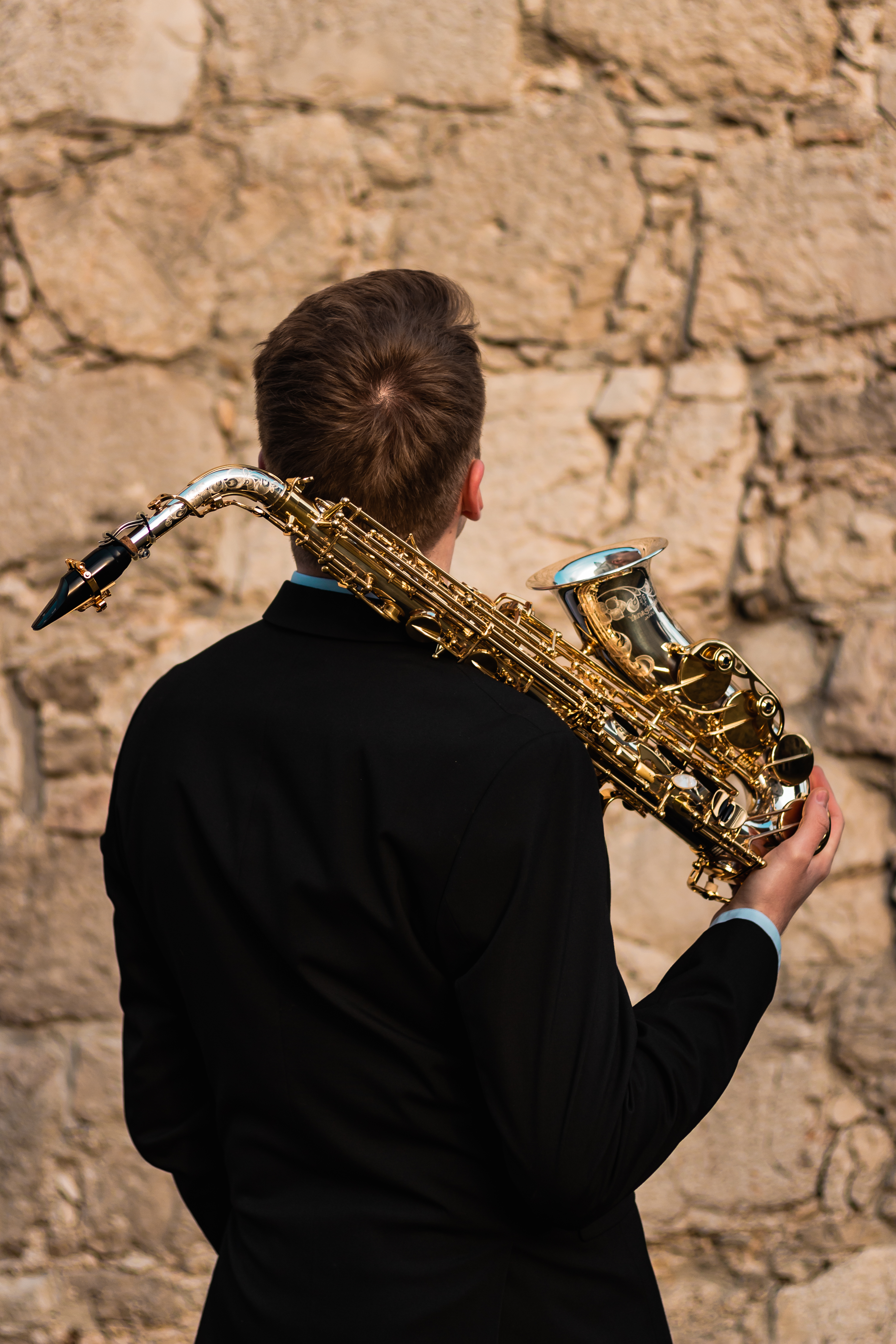 A man in a black suit is holding a saxophone.