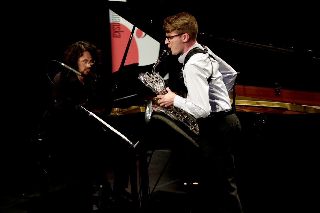 Two musicians playing music: one is on a traditional piano and the other would be playing the saxophone. The sheet music i...